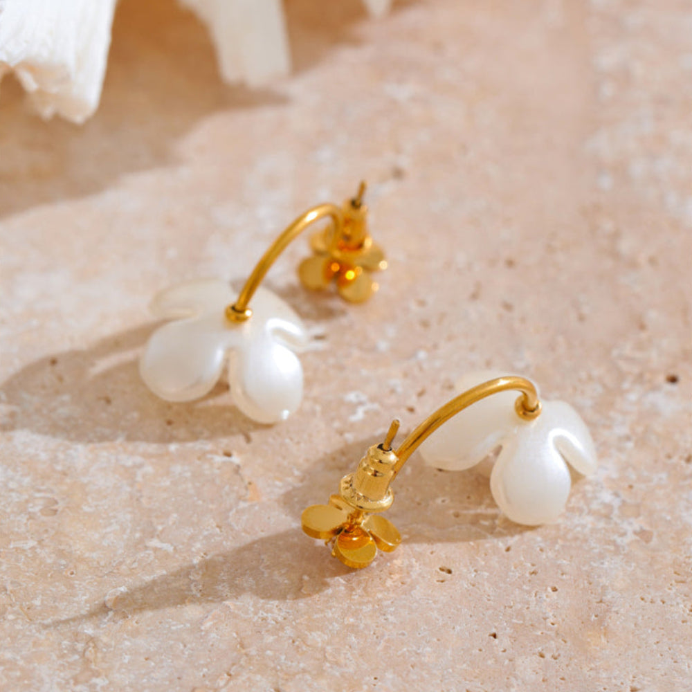 Gold and pearl earrings on a textured beige surface.  latest earring models and trending earrings models. new arrivals.