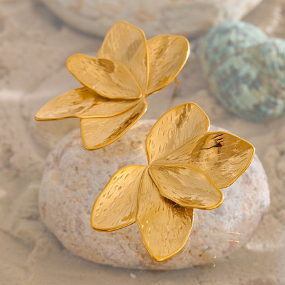 Gold flower-shaped earrings on a textured surface. latest earring models and trending earrings models. new arrivals.