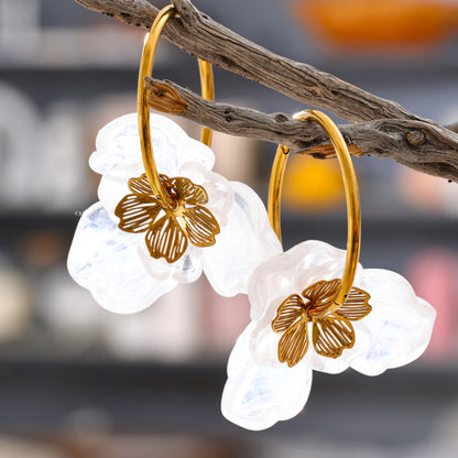 Gold hoop earrings with white floral designs on a branch against a blurred background. latest earring models and trending earrings models. new arrivals.