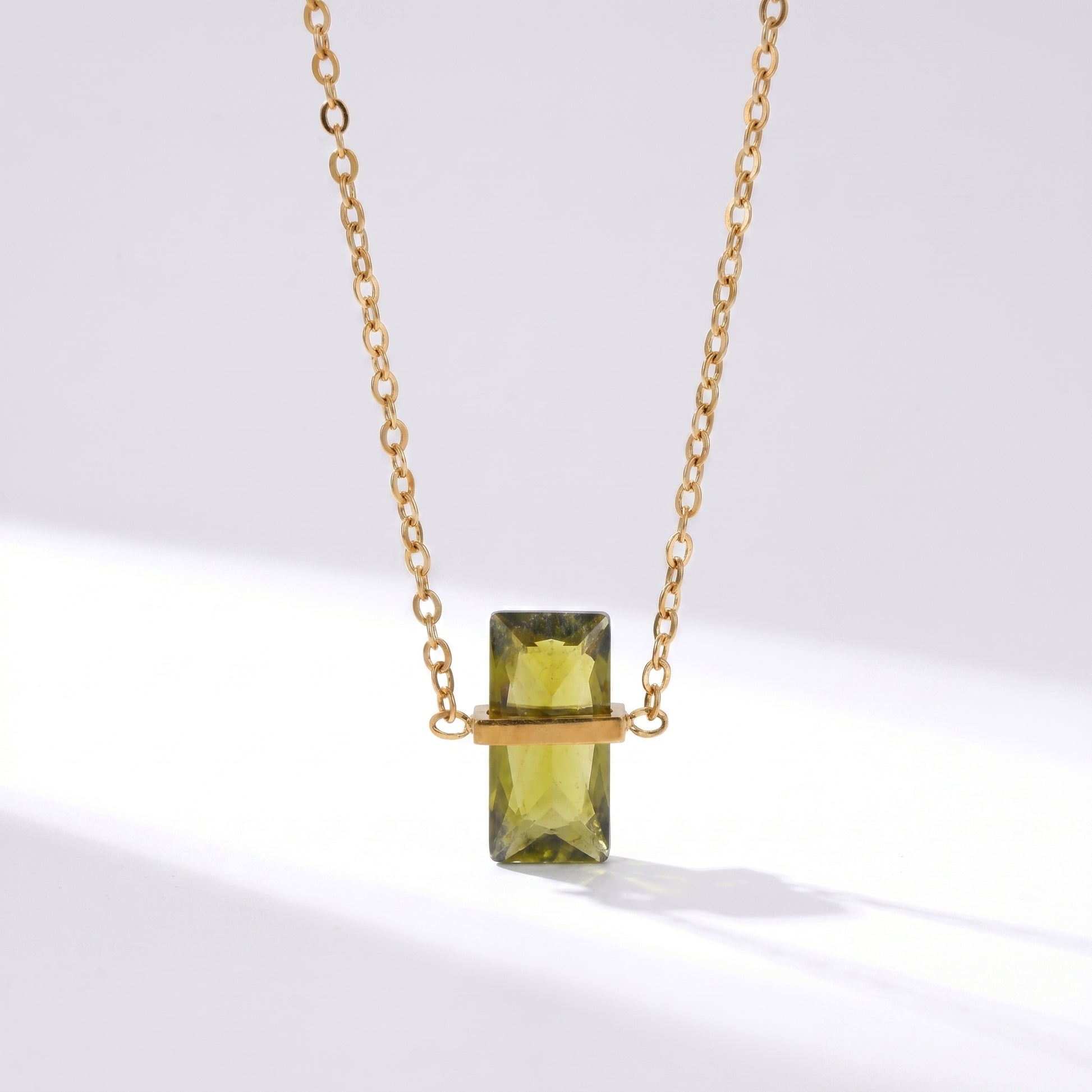 Gold necklace with a green rectangular gemstone on a white background