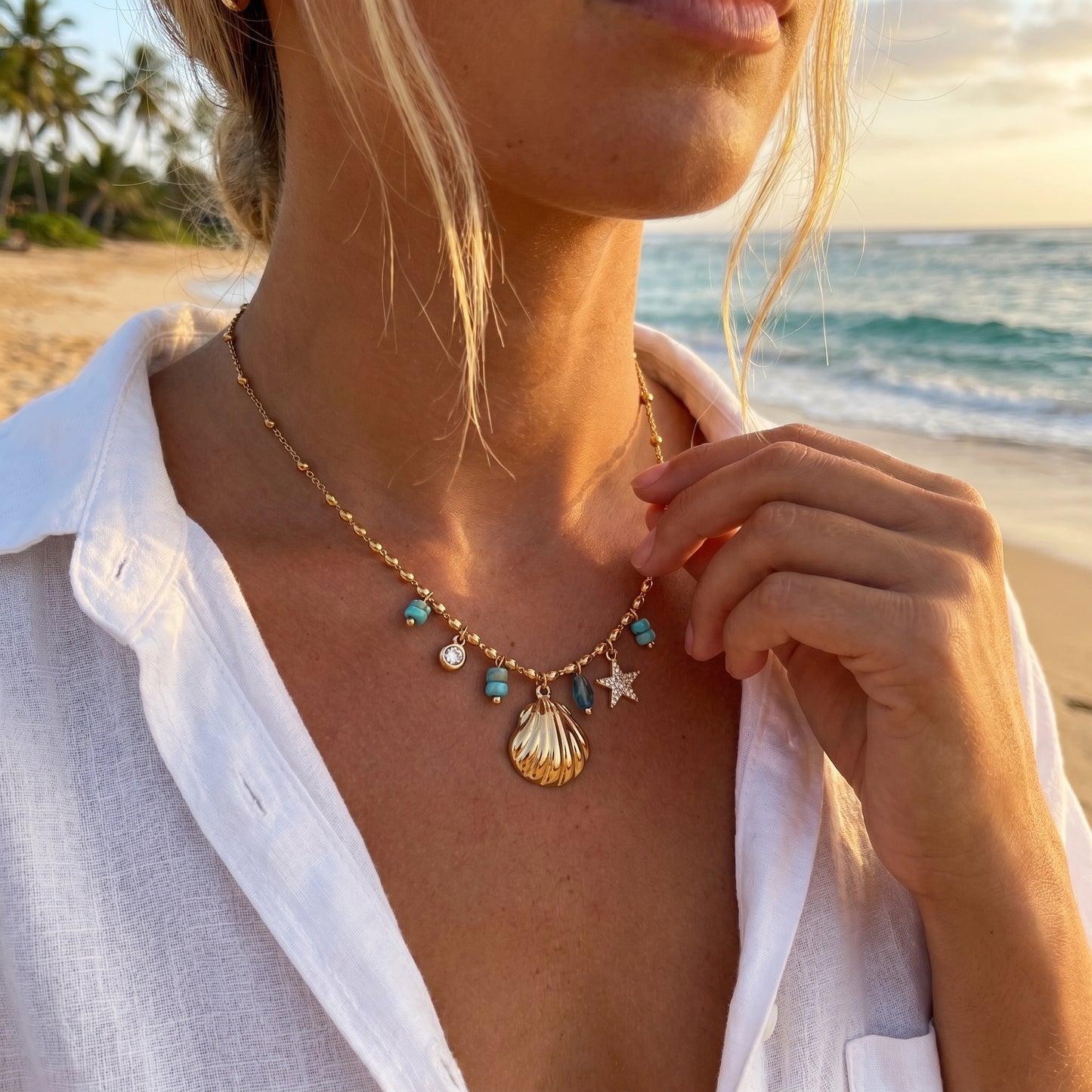 Person wearing a necklace with seashell and star charms on a beach at sunset
