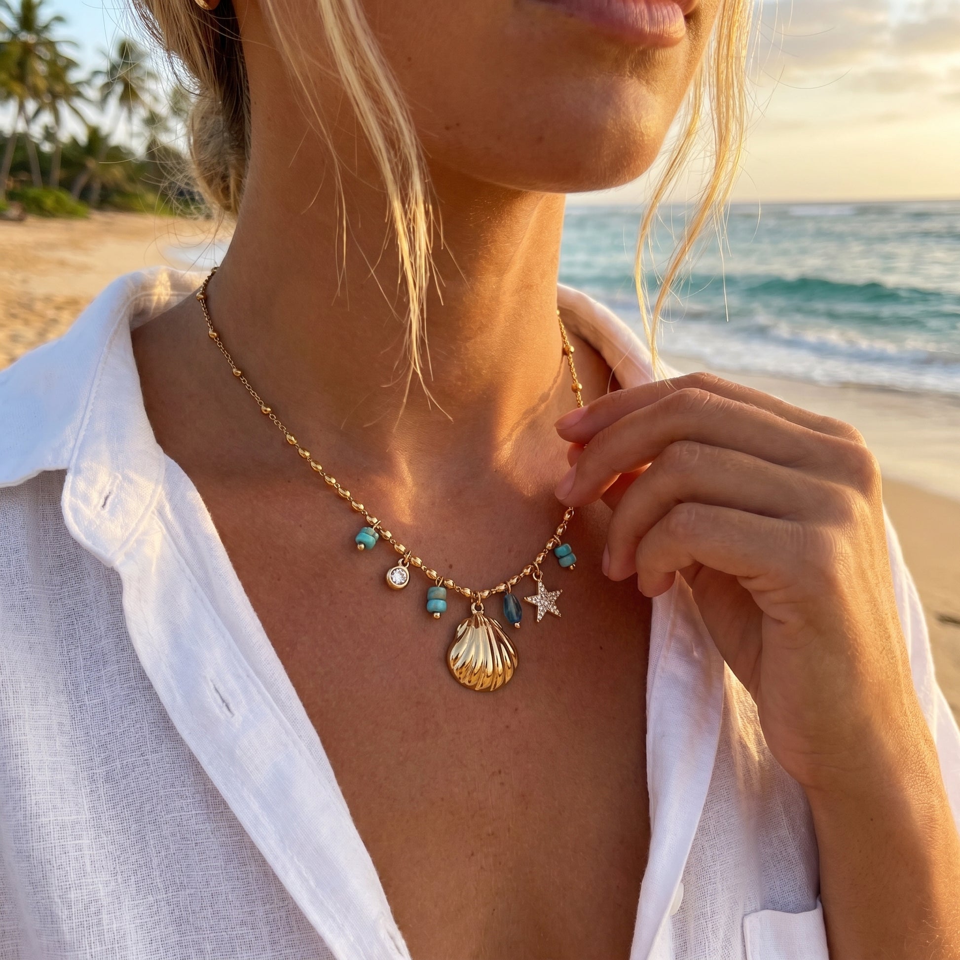 Person wearing a necklace with seashell and star charms on a beach at sunset