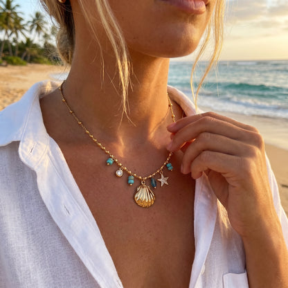 Person wearing a necklace with seashell and star charms on a beach at sunset