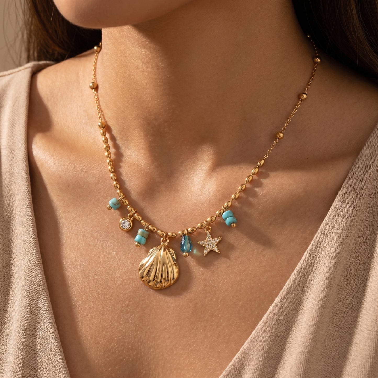 Waterproof gold-plated coastal charm necklace by Floravisha, laid flat on a white background. The delicate beaded chain features a shiny gold seashell pendant, a crystal-encrusted starfish, and vibrant turquoise bead accents.