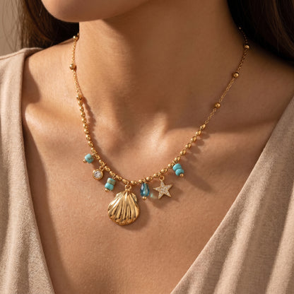 Waterproof gold-plated coastal charm necklace by Floravisha, laid flat on a white background. The delicate beaded chain features a shiny gold seashell pendant, a crystal-encrusted starfish, and vibrant turquoise bead accents.