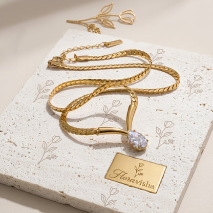 Gold snake chain necklace with teardrop crystal pendant, minimalist adjustable jewelry for women on textured background.
