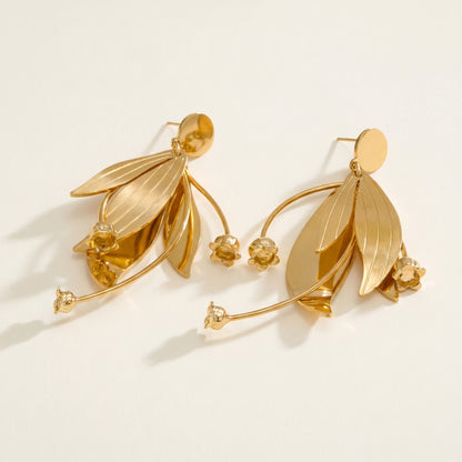 Gold leaf-shaped earrings on a light beige background