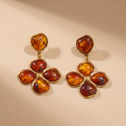 Close-up of luxury amber floral drop earrings resting on a warm beige matte surface, highlighting the tarnish-free gold plating and rich tortoiseshell resin details.
