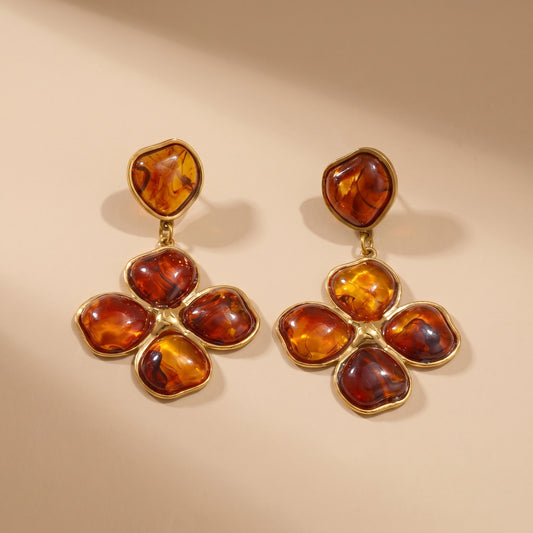 Close-up of luxury amber floral drop earrings resting on a warm beige matte surface, highlighting the tarnish-free gold plating and rich tortoiseshell resin details.