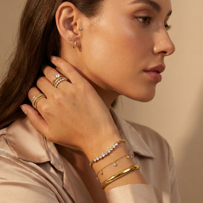 Woman wearing gold jewelry including earrings, rings, and bracelets on a beige background