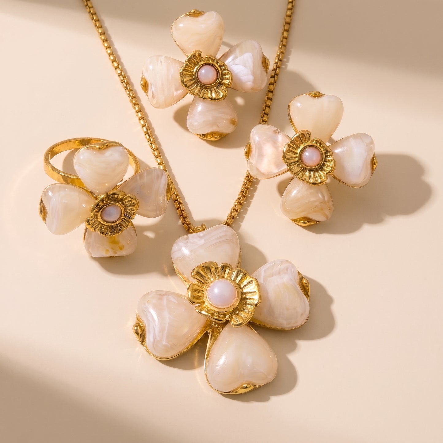 The high quality Fleur Bloom Pendant Necklace in Cream Alabaster by Floravisha, showing the marbled resin flower pendant and gold box chain next to matching earrings and ring.