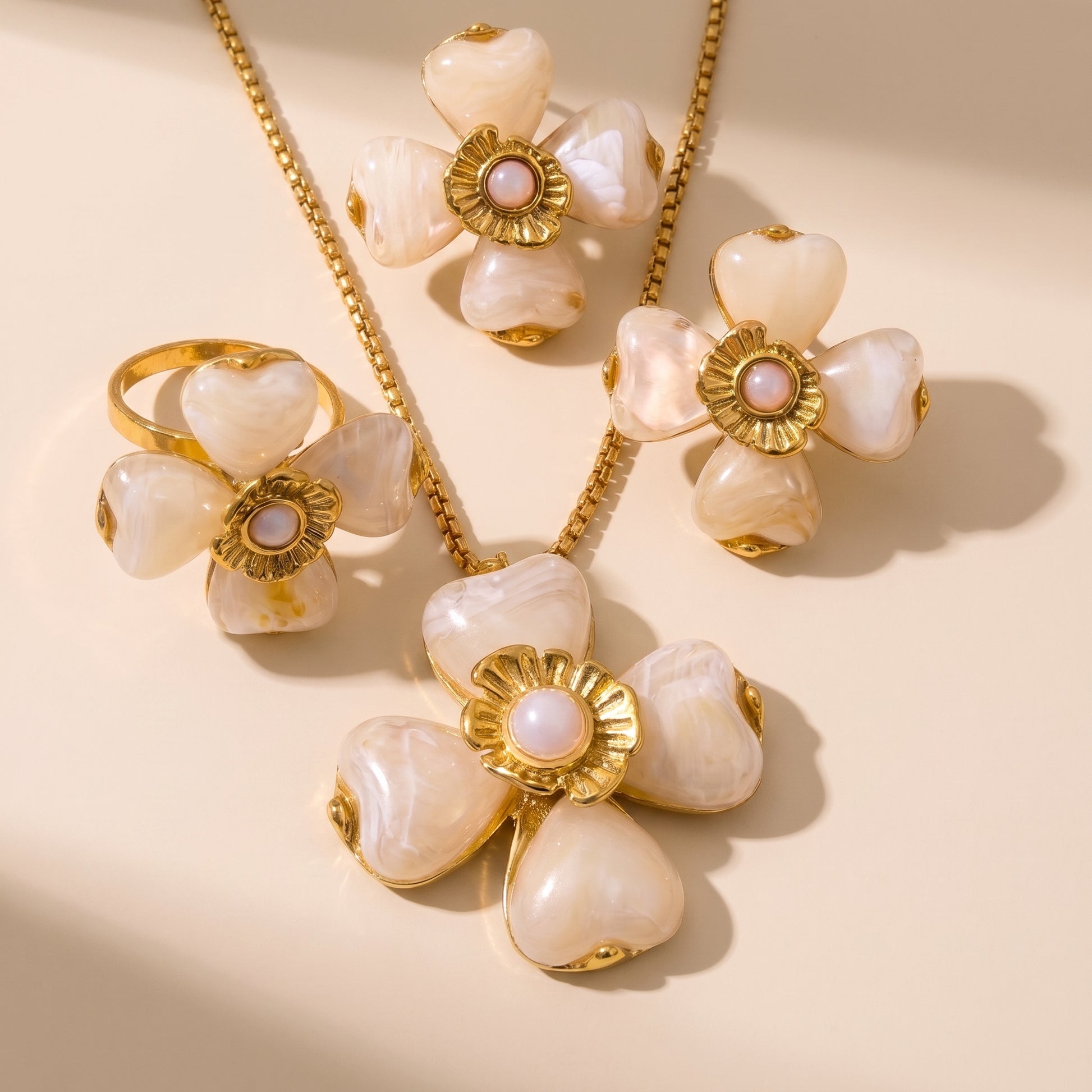 The high quality Fleur Bloom Pendant Necklace in Cream Alabaster by Floravisha, showing the marbled resin flower pendant and gold box chain next to matching earrings and ring.