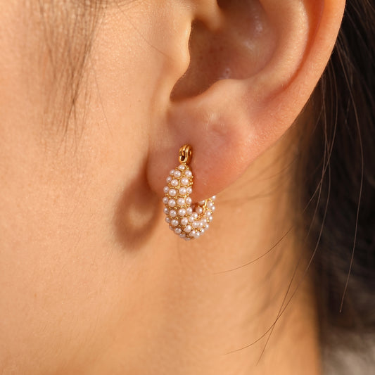 Close up side profile view of a model wearing the skin friendly Lumina gold pearl huggie hoops, highlighting their comfortable fit on the earlobe.
