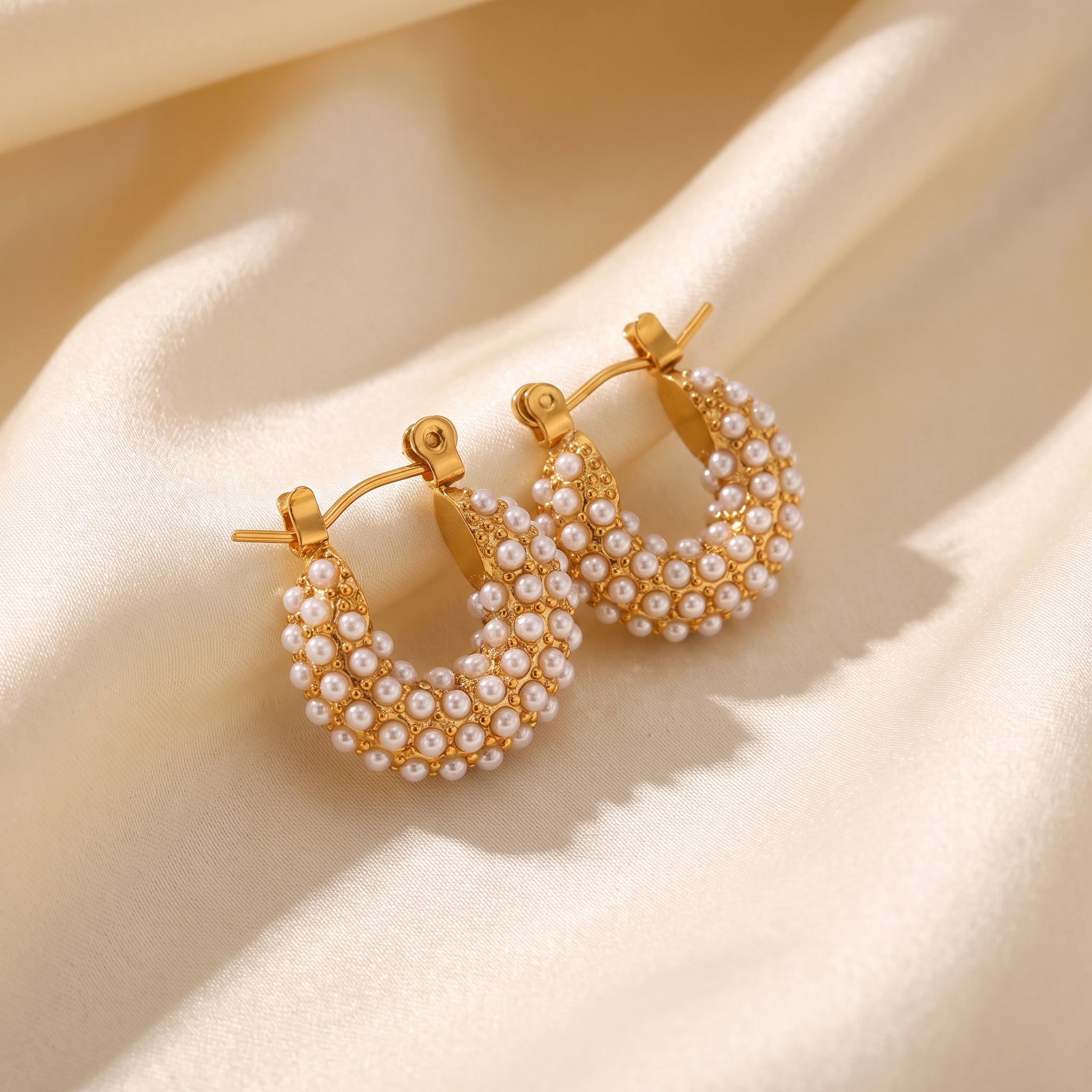 The high quality Lumina Micro Pearl Pavé Hoops by Floravisha, featuring encrusted seed pearls and gold PVD plating on draped cream satin fabric.