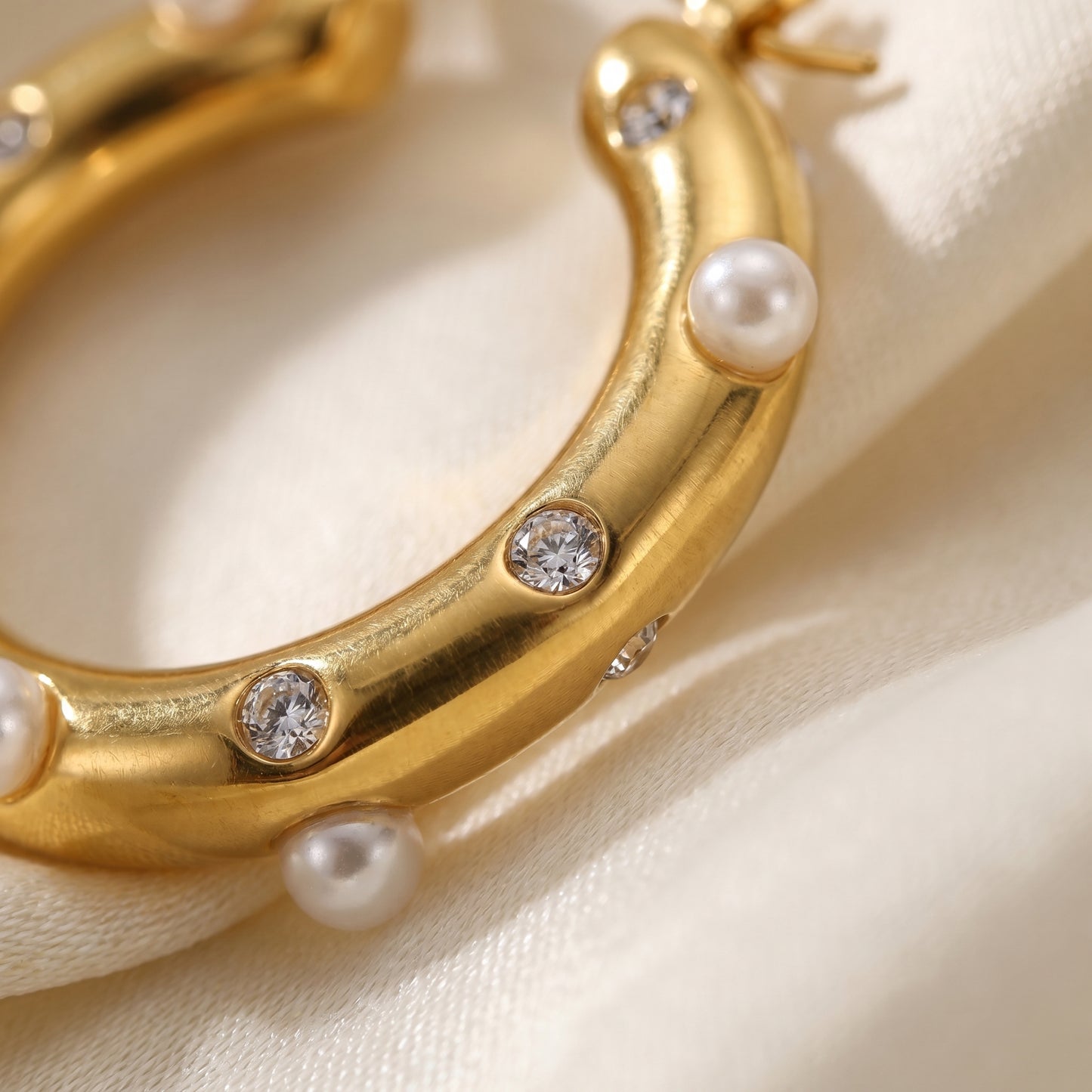 Gold hoop earring with pearls and crystals on a beige background.