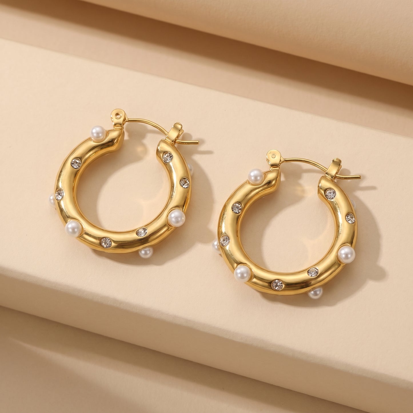 Gold hoop earrings with pearls and small diamonds on a beige background.