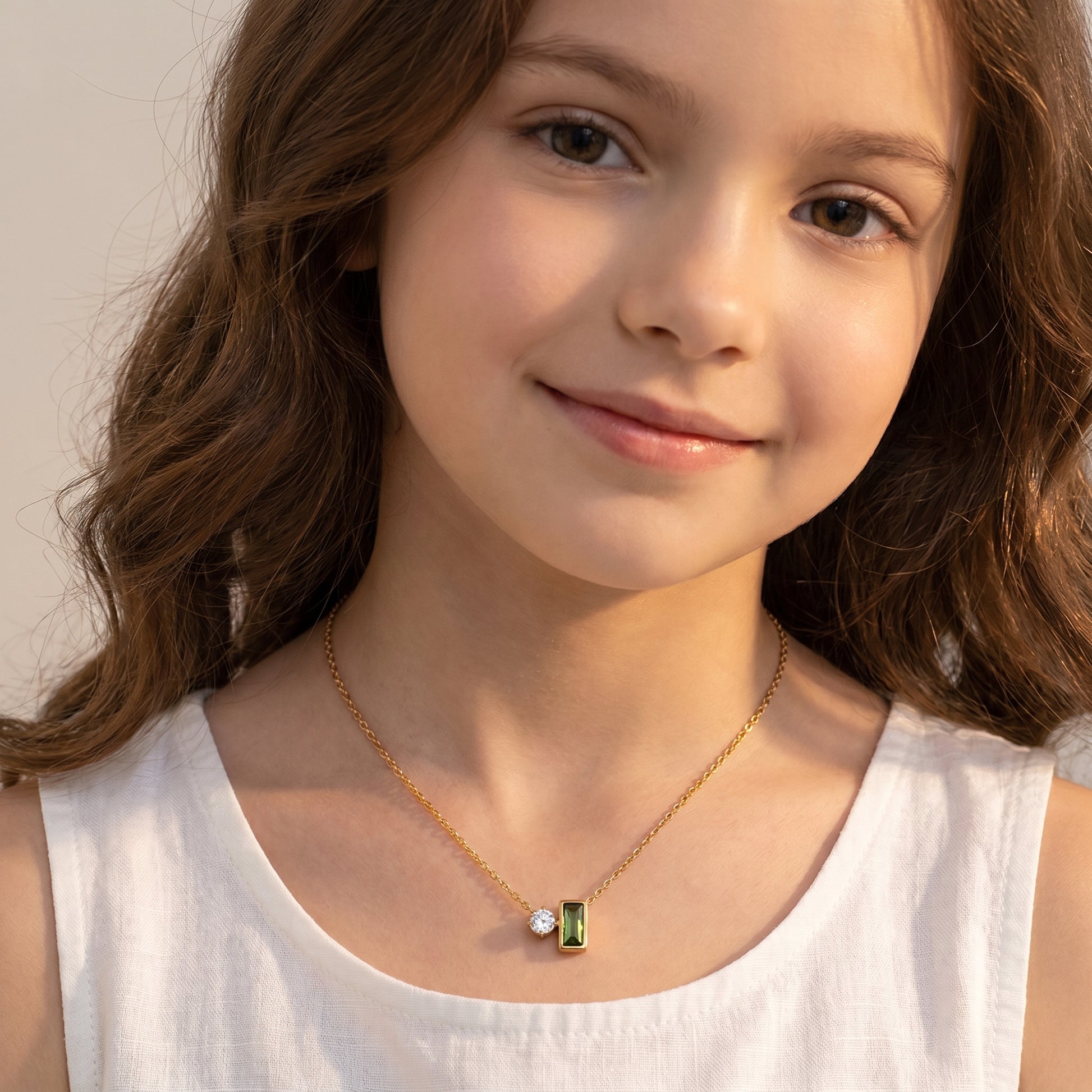 Young girl wearing a gold necklace with a green pendant against a neutral background