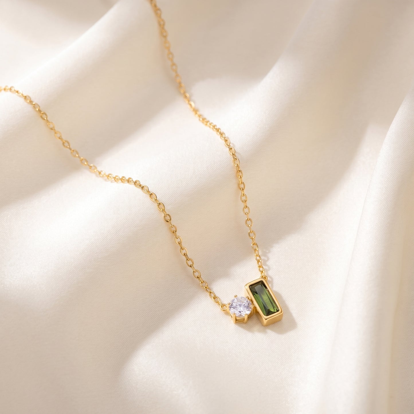 Gold necklace with green gemstone pendant on a beige fabric background