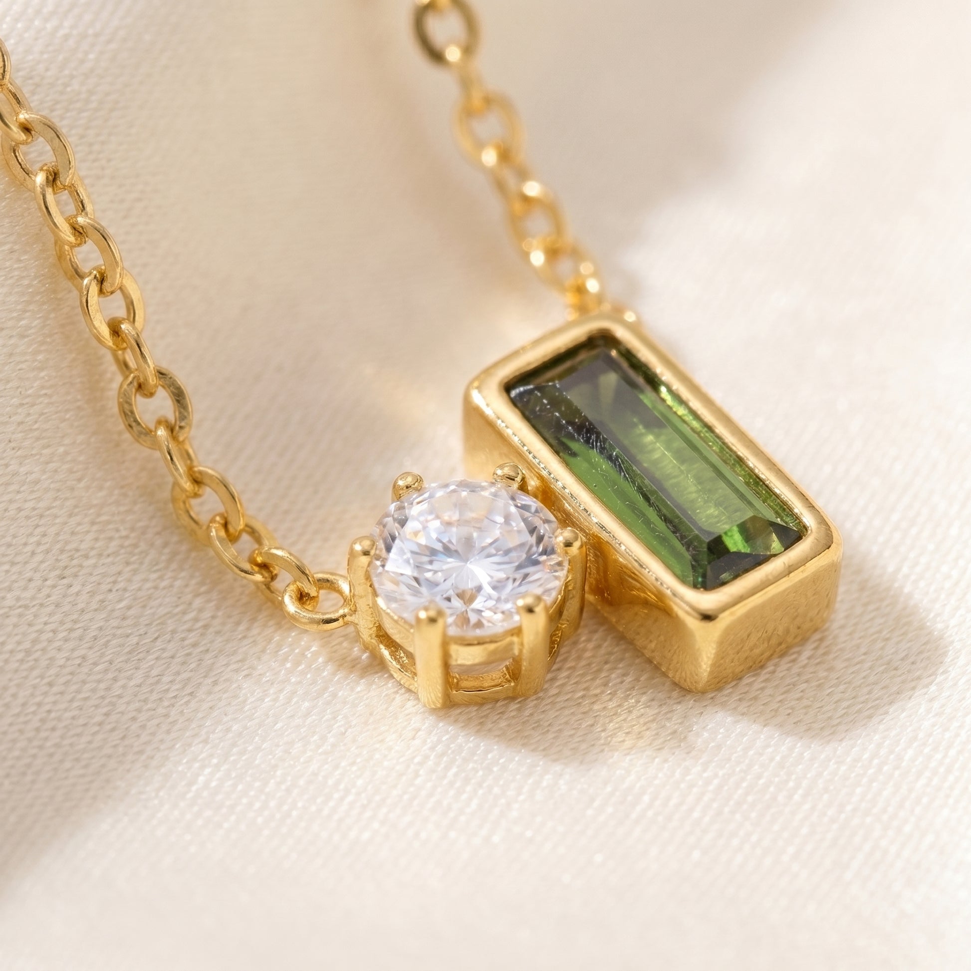 Gold necklace with a green gemstone and clear gemstone on a beige fabric background