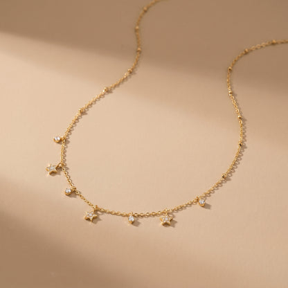 Dainty gold beaded satellite chain necklace featuring alternating dangling mini starburst charms and clear crystal drops on a clean white background, highlighting its tarnish-free and skin friendly finish on a beige background