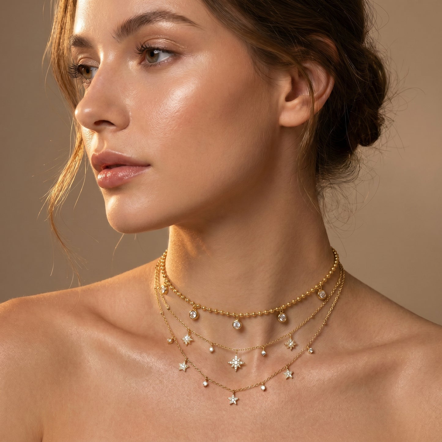 Close-up of a woman wearing Dainty gold beaded satellite chain necklace featuring alternating dangling mini starburst charms and clear crystal drops, highlighting its tarnish-free and skin friendly finish against a neutral background.