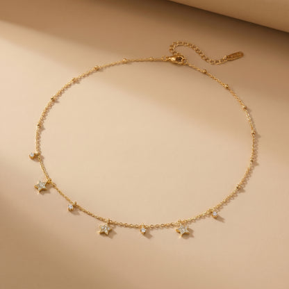 Dainty gold beaded satellite chain necklace featuring alternating dangling mini starburst charms and clear crystal drops. highlighting its tarnish-free and skin friendly finish on a beige background