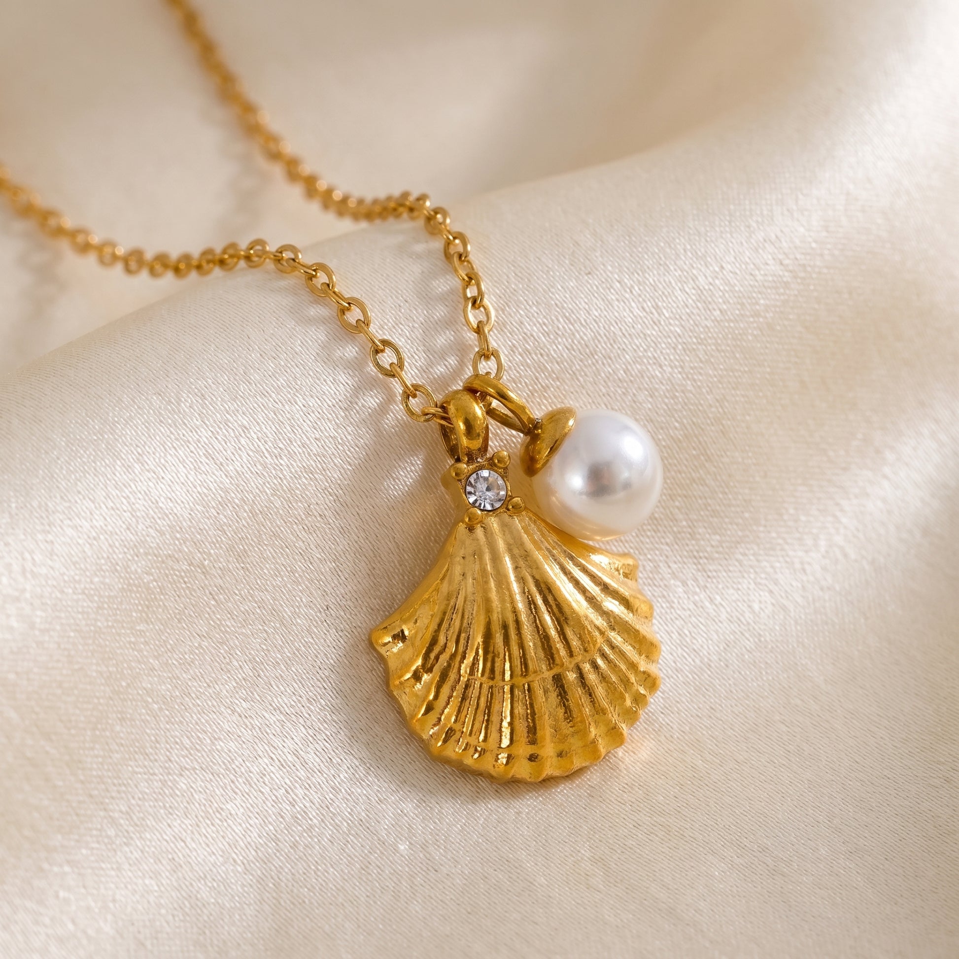 Gold necklace with scallop shell and pearl pendant on a beige fabric background