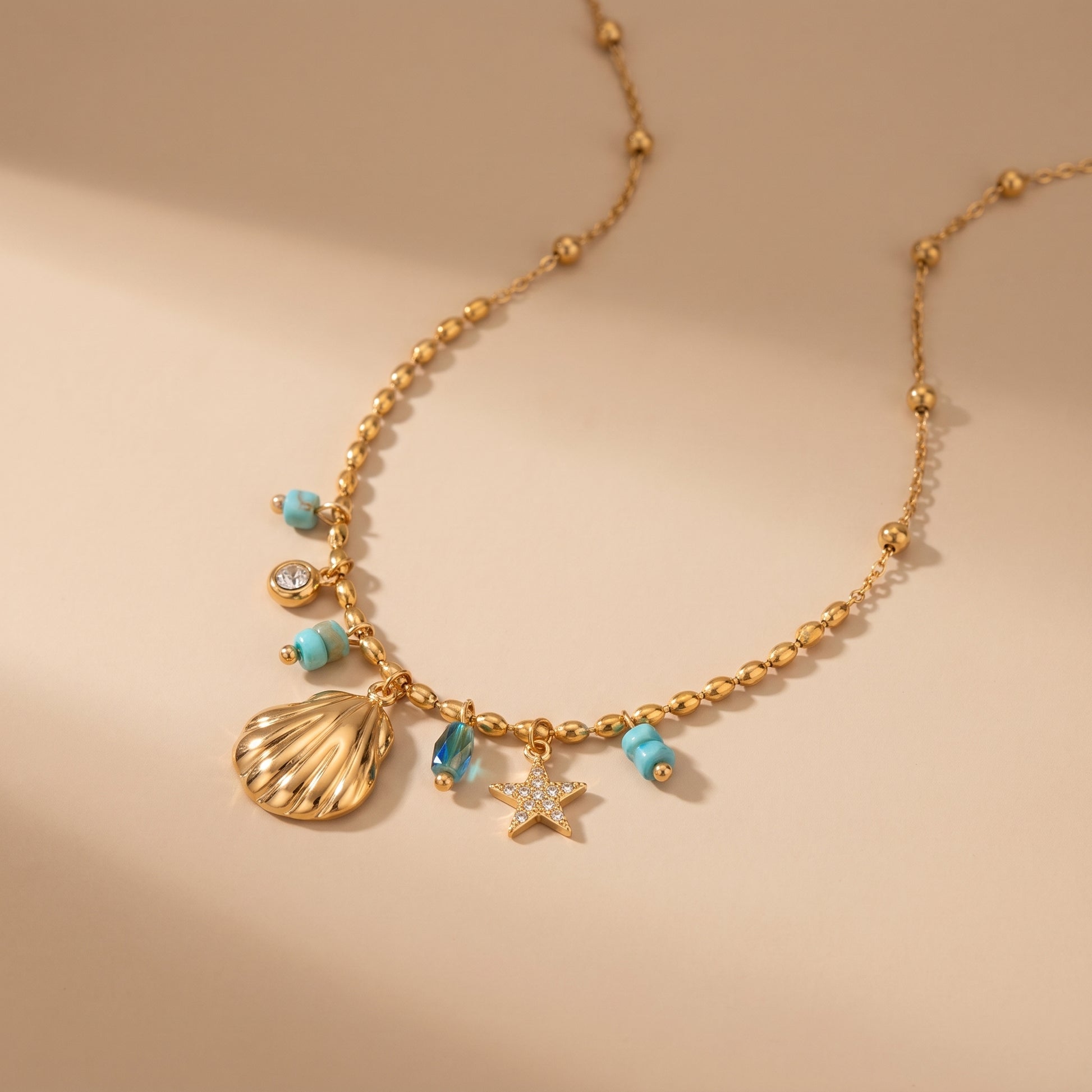 Gold necklace with shell and starfish charms on a beige background