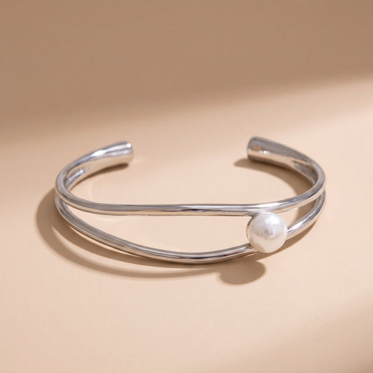 The tarnish-free Oceane Wave Pearl Cuff Bangle by Floravisha, displaying two fluid asymmetrical platinum bands wrapping a lustrous white pearl on a clean background