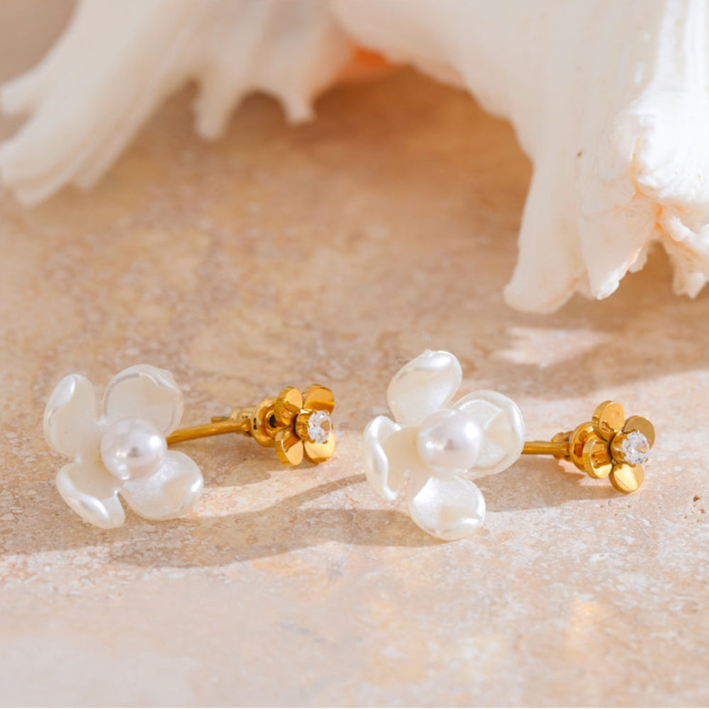 Pair of gold and pearl flower-shaped earrings on a textured beige surface. latest earring models and trending earrings models. new arrivals.