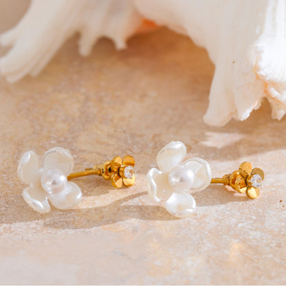 Pair of gold and pearl flower-shaped earrings on a textured beige surface. latest earring models and trending earrings models. new arrivals.