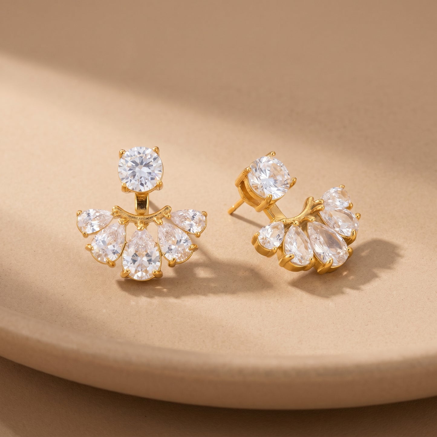 High quality waterproof gold plated 2-in-1 convertible fan earrings featuring a round solitaire stud and an interchangeable fanned crescent of clear crystals, on a beige background.
