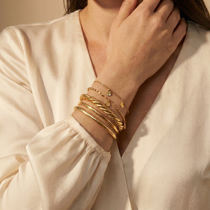 Close-up of a person wearing  high quality Sienne Twisted Cuff Bangle by Floravisha on a beige background.