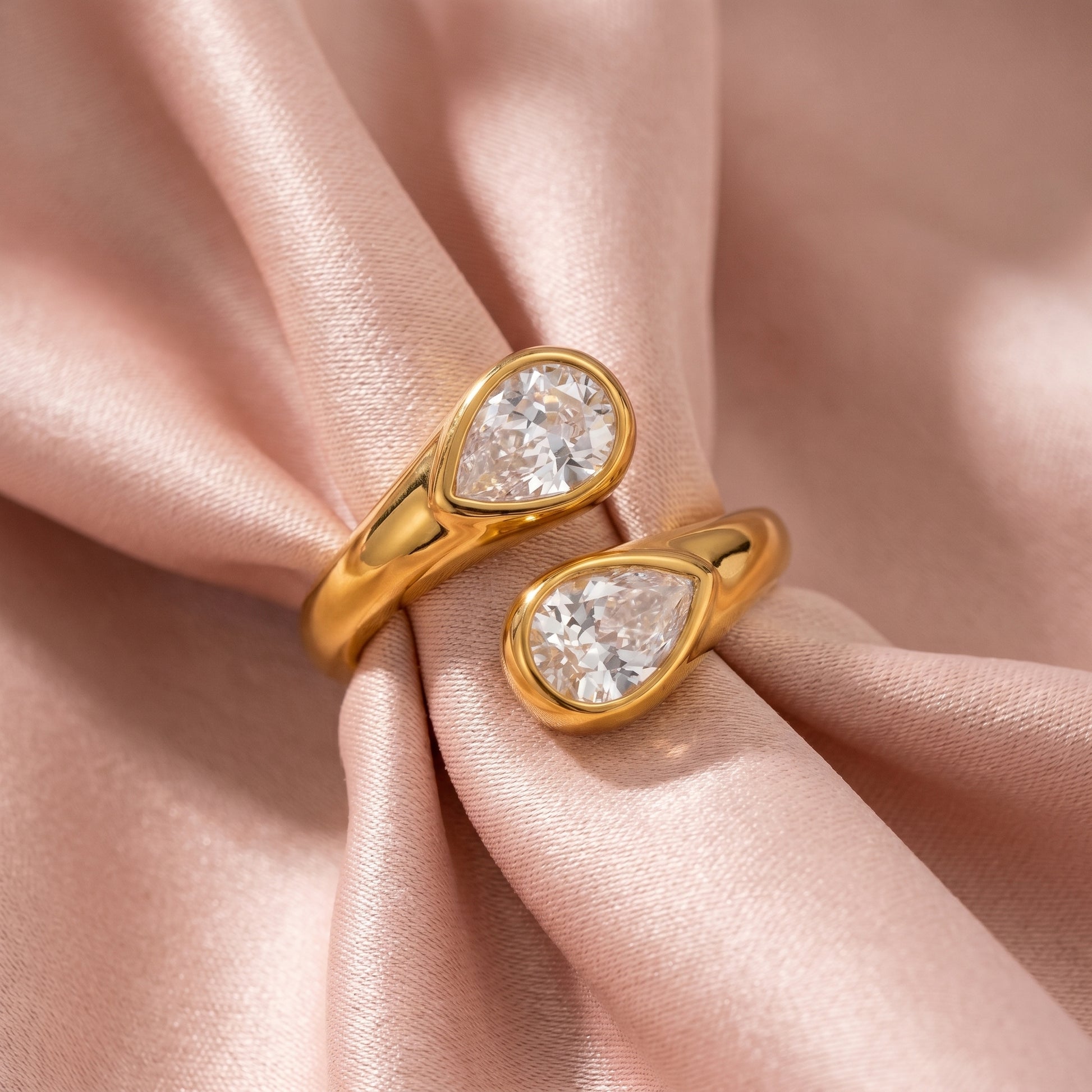 Soleil Toi et Moi Adjustable Ring by Floravisha. A high quality, waterproof gold plated open wrap ring featuring two brilliant teardrop-cut clear crystals. Elegant, tarnish-free, and skin friendly on a soft pink fabric background.