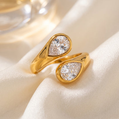 Soleil Toi et Moi Adjustable Ring by Floravisha. A high quality, waterproof gold plated open wrap ring featuring two brilliant teardrop-cut clear crystals. Elegant, tarnish-free, and skin friendly on a soft beige fabric background.