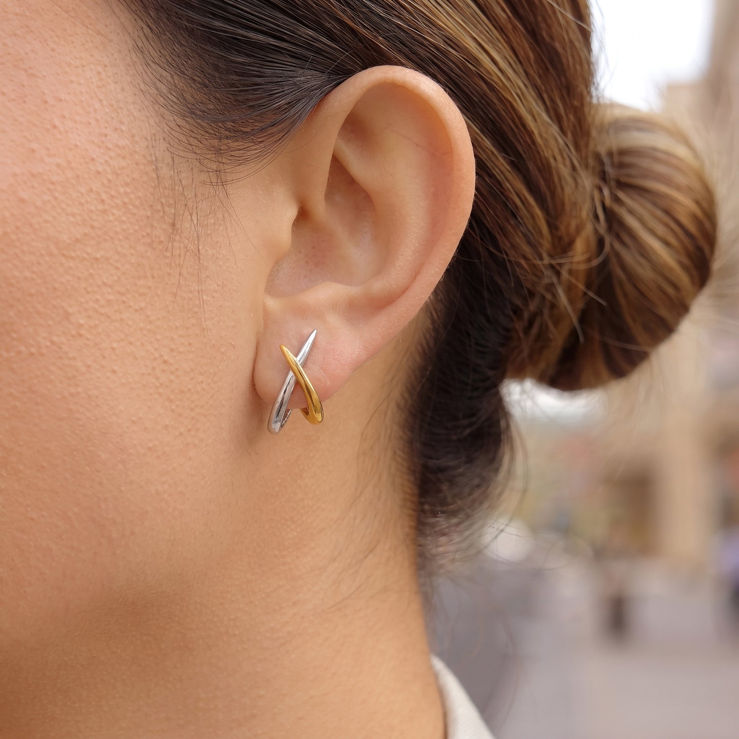 A close-up of a person's ear wearing a Two-Tone Crossover Hoop Earrings - Waterproof Gold & Silver | Floravisha