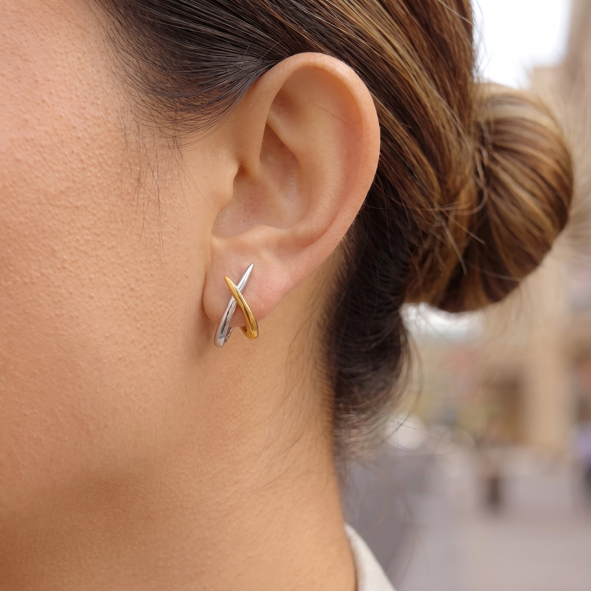 A close-up of a person's ear wearing a Two-Tone Crossover Hoop Earrings - Waterproof Gold & Silver | Floravisha