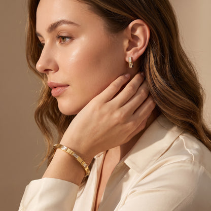 Close-up side profile of a woman wearing the skin friendly Verona gold bezel bracelet and matching crystal huggie studs with a cream silk blouse.