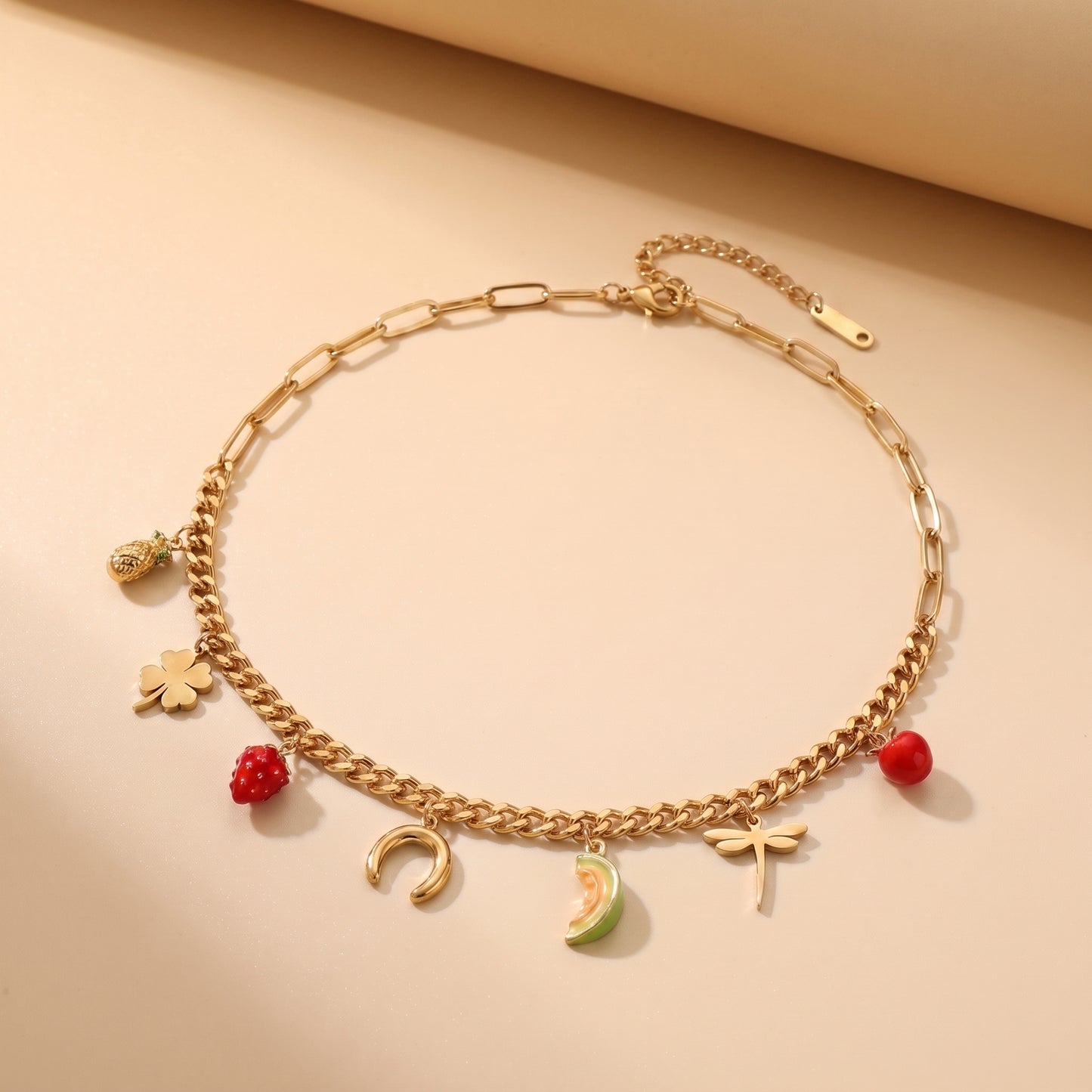 The high quality Verona Eclectic Charm Necklace by Floravisha, displaying its dual paperclip and curb chains with strawberry, clover, dragonfly, and apple charms lying flat on a clean  background.