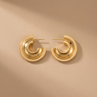 Sleek, high quality Vesper Arch gold dome hoops shown side-by-side on a reflective beige background, highlighting their brilliant waterproof gold plating.