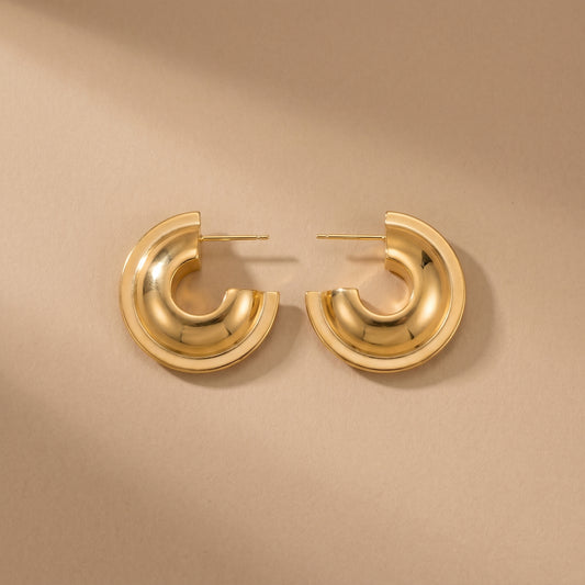 Sleek, high quality Vesper Arch gold dome hoops shown side-by-side on a reflective beige background, highlighting their brilliant waterproof gold plating.