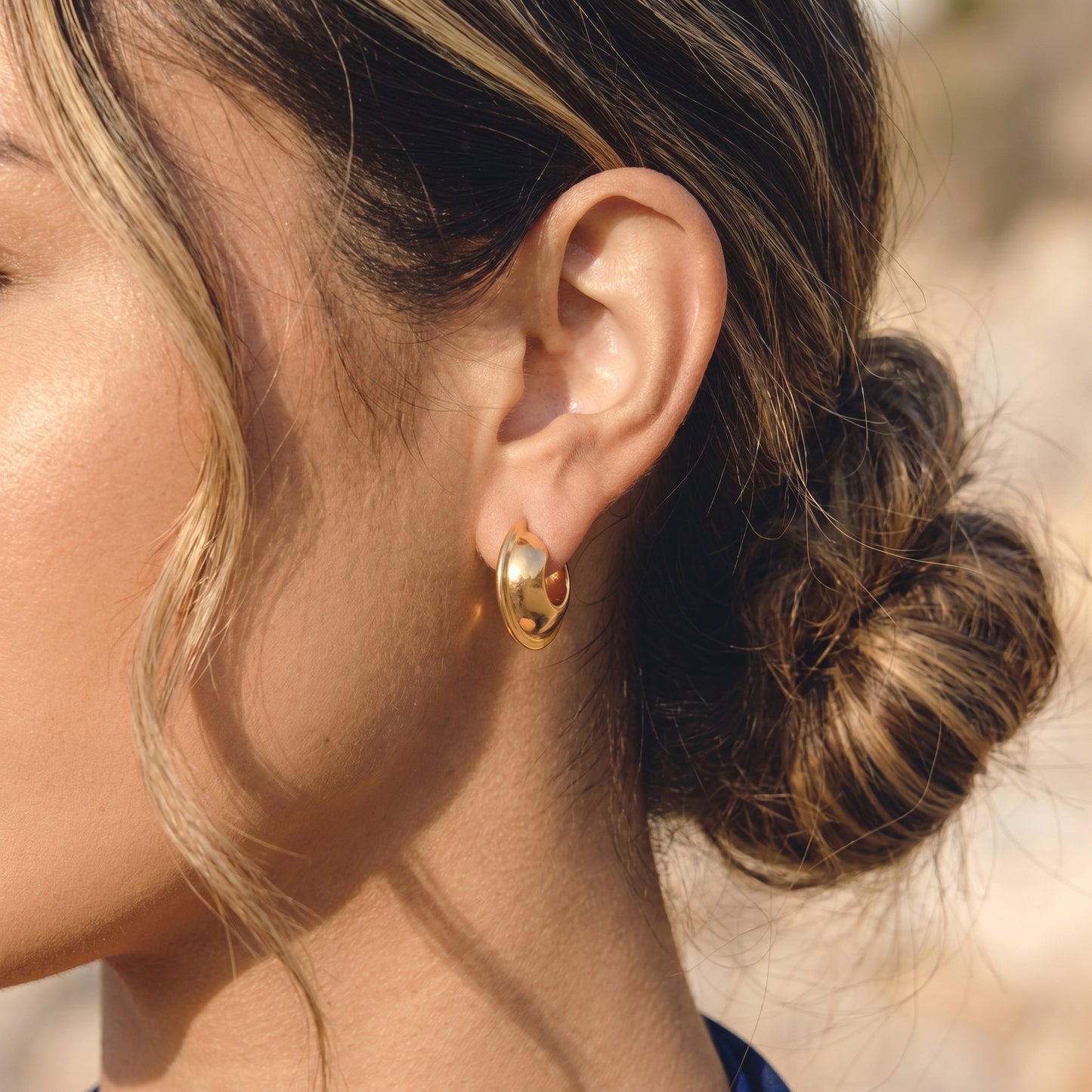 Close up side profile view of a model wearing the Vesper Arch gold hoops by Floravisha, highlighting their skin friendly construction and warm golden reflection.