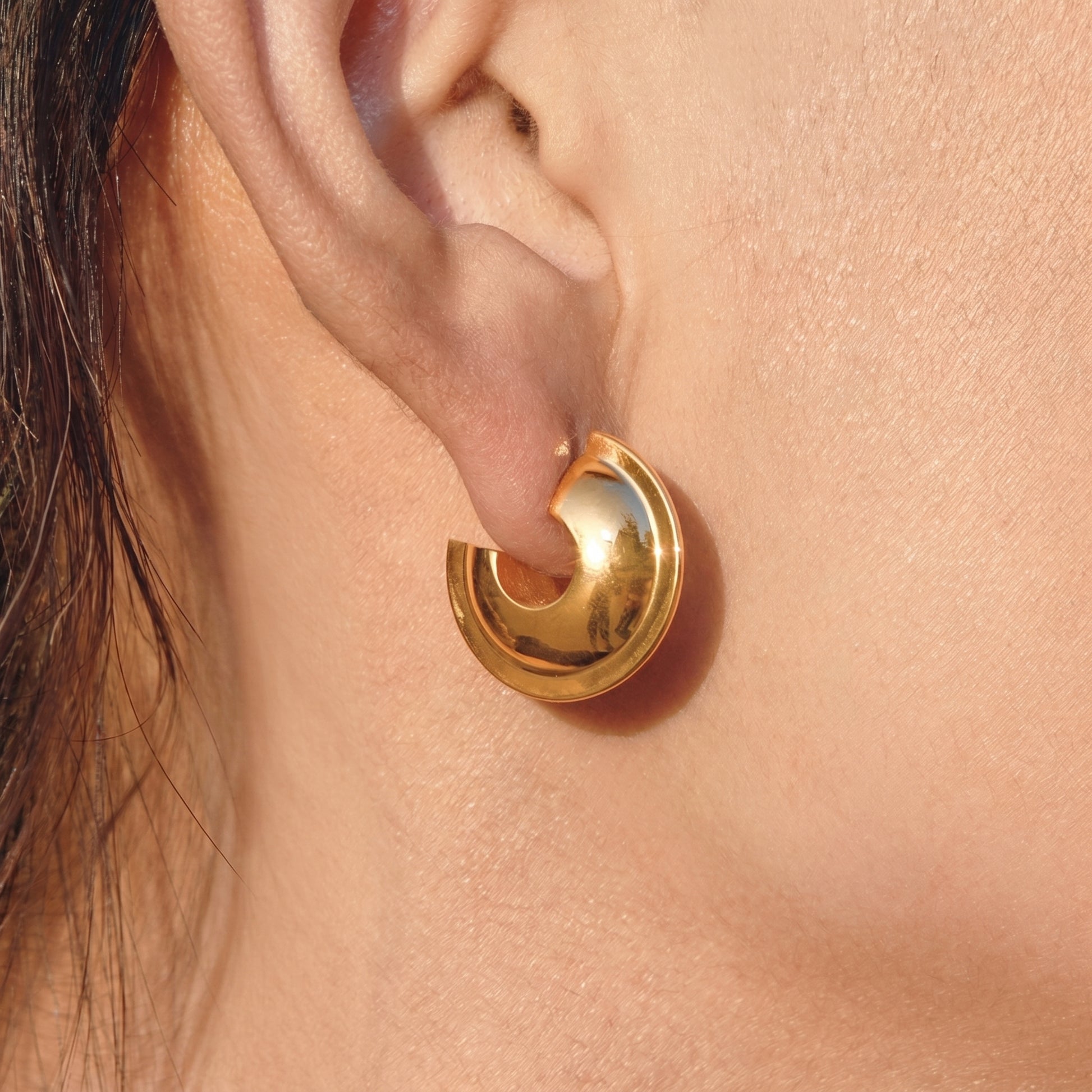 Close up side profile view of a model wearing the Vesper Arch gold hoops by Floravisha, highlighting their skin friendly construction and warm golden reflection.