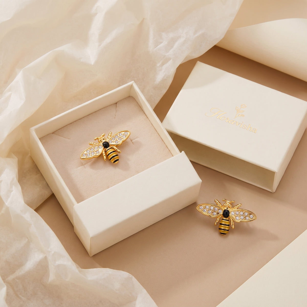 Pair of tarnish-free Abeille gold pavé honeybee stud earrings displayed inside a warm-white Floravisha embossed drawer jewelry gift box.