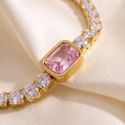 Extreme macro close-up of the tarnish-free Amara gold tennis bracelet showcasing the bezel-set pink emerald-cut crystal on champagne silk.