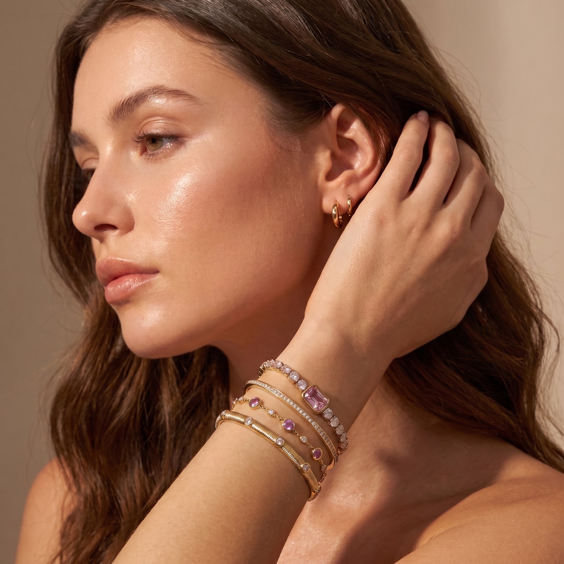 Modern gold wrist stack on a woman featuring the skin friendly Amara pink tennis bracelet paired with delicate gemstone and cuff bangles.