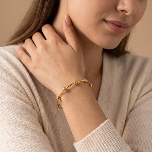 Editorial portrait of a woman wearing the tarnish-free Astrid gold beaded cuff bangle styled with an oatmeal knit sweater in soft lighting.