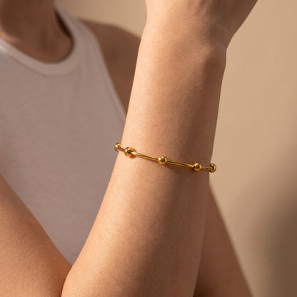 Close-up view of a woman's wrist wearing the skin friendly Astrid gold beaded open cuff bangle paired with a white ribbed top.