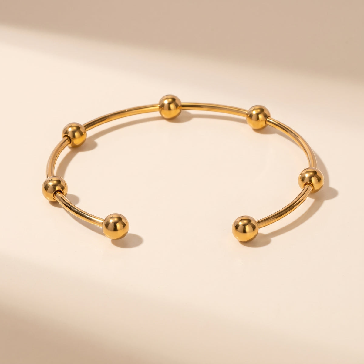 High quality Astrid gold beaded cuff bangle by Floravisha showing mirror-polished spheres and open wire design on a warm beige studio surface.