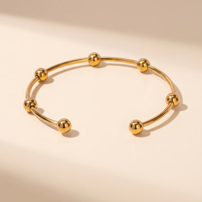 High quality Astrid gold beaded cuff bangle by Floravisha showing mirror-polished spheres and open wire design on a warm beige studio surface.